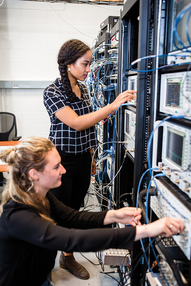 Yamoah (standing) and a fellow researcher adjust controls on instruments connected to the dilution refrigerator in which they conduct experiments on qubit devices. Photo courtesy of Nathan Fiske.